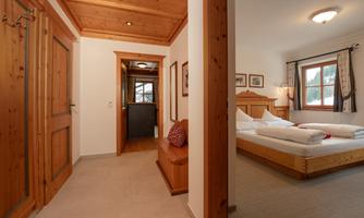 A cozy room with wooden paneling and a large bed. The entrance displays an inviting atmosphere with natural light.