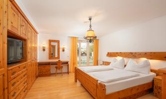A cozy bedroom with wooden furniture and a large window. The decor is bright and inviting, featuring a double bed and a desk.