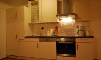 A modern kitchen with white cabinets and a black countertop. There is a stove, a sink, and some kitchen appliances.