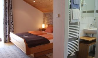 A cozy bedroom with a double bed and warm colors. The bathroom is modern and bright, with a shower and a beautiful wooden shelf.