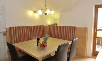 A cozy dining area with a wooden table and comfortable chairs. On the table, there is a bowl of fruit and two glasses.