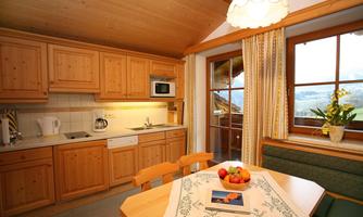 A cozy kitchen with wooden cabinets and modern appliances. A dining table stands in the center, decorated with fruit and a blooming plant by the window.