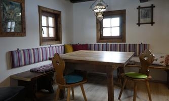 A cozy dining area with a wooden tray and colorful cushions. The walls are plain, and there are two windows that let in natural light.