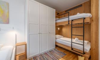 A modern bedroom with a bunk bed and a wardrobe. The room has a bright, cheerful atmosphere with a colorful carpet.