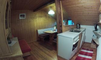 A cozy kitchen area in a wooden apartment. The room features a dining area, a kitchen corner, and warm wood design.