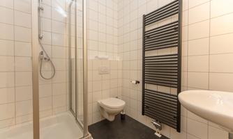 A modern bathroom with a shower, a sink, and a toilet. The walls are brightly tiled, and a towel radiator is also present.