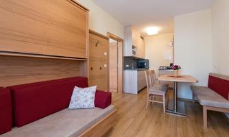 A modern kitchen-living room with wood interiors and red accents. The space is bright and inviting, with a dining area and a sofa.
