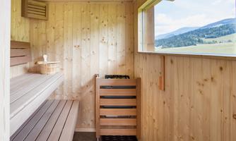 A bright sauna with wooden interior and a window that offers a view of the landscape. The benches are made of light wood and invite relaxation.