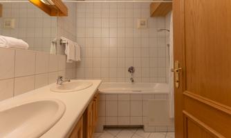 A clean bathroom with two sinks and a bathtub. The walls are brightly tiled and there are fresh towels.