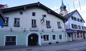 A traditional building with green paint and several windows. Next to the house, you can see a clock tower and another building.