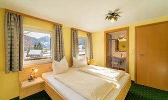 Cozy bedroom with a double bed and large windows offering a view of the mountains. The room is brightly and cheerfully decorated.