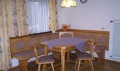 A cozy dining area with a wooden table and benches. The walls are decorated with yellow curtains and a clock hangs on the wall.