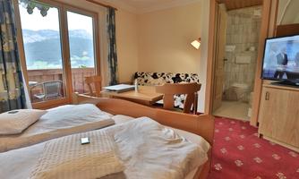 A cozy bedroom with two beds and a small living area.  
Windows offer a view of the mountains, and a television is also available.