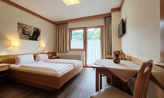A cozy room with two beds and a small table. Large windows provide plenty of daylight.