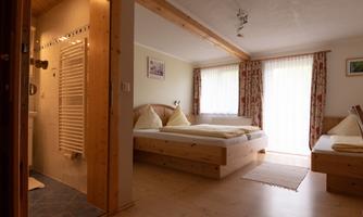 A cozy room with wooden furniture and two beds. Large windows provide plenty of daylight.