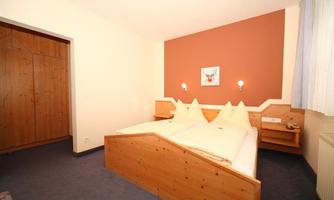 A cozy bedroom with two single beds and light wood accents. The walls are painted in warm colors and there is a pleasant lighting.