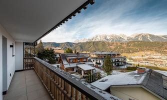 A terrace with a view of the mountains and the valley. Surrounded by modern houses and trees.