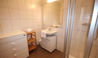 A modern bathroom with bright tiles and clean lines. There is a shower, a sink, and storage space.