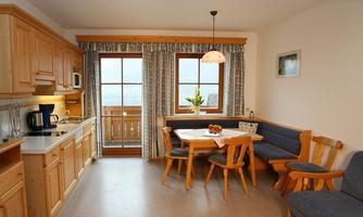 A cozy kitchen with wooden cabinets and a dining table. Large windows provide a view outside and plenty of natural light.