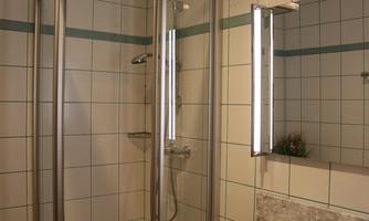 A modern bathroom with a shower cubicle and a sink. The walls are tiled and there is bright lighting.