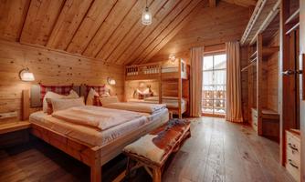 A cozy room in a wooden style with two beds and a bunk bed. Large windows provide lots of daylight and a beautiful view.