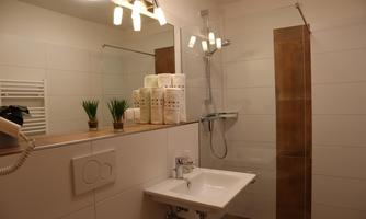 A modern bathroom with a shower and a sink. Towels and small plants are on the shelf.