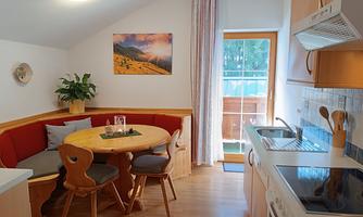 A cozy kitchen with a round table and a red bench. The room has large windows that let in plenty of light.