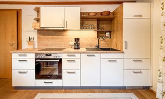 A modern kitchen with white cabinets and wooden accents. The equipment includes a stove, a sink, and various kitchen utensils.