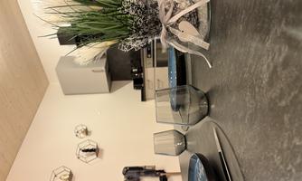 A modern kitchen with a decorative table. On the table are glasses, plates, and a blooming plant pot.