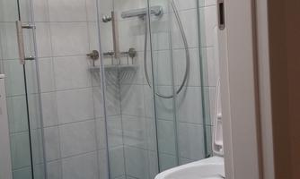 A modern bathroom with a glass shower and a simple toilet. The floor is designed with blue tiles.