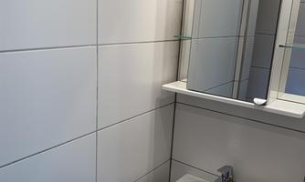 A modern bathroom with white tiles and a small sink. A mirror and a towel complete the space.