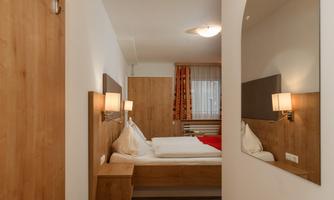 A modern bedroom with wood paneling and soft light fixtures. The room is bright and cozy, featuring a large mirror and a red accent.