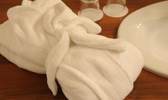 A soft, white bathrobe lies on a wooden table. Next to the bathrobe are two glasses and a plate.