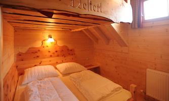 A cozy wooden holiday room with a double bed and warm light. The walls are made of light wood, creating an inviting atmosphere.