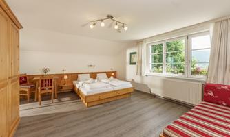 A bright and cozy room with a double bed and an additional sleeping space. The room features a table, chairs, and large windows overlooking the outdoors.