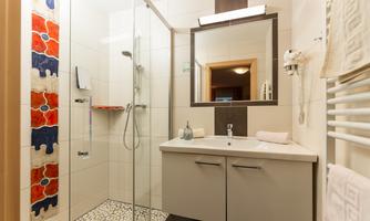 A modern bathroom with a walk-in shower and an elegant sink. The walls are designed with decorative tiles in blue and orange.