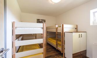 A simple bedroom with two bunk beds and a wardrobe. The walls are light and the floor is made of wood.