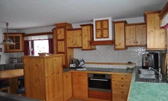 A cozy kitchen with wooden furniture and a modern stove. The room is bright and inviting, ideal for cooking and socializing.