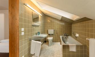A modern bathroom with a bathtub, a toilet, and a sink. The walls are decorated with yellow tiles and there is a skylight.