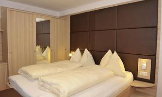 A modern bedroom with a double bed and two large pillows. The walls are painted in neutral colors, and there is a built-in wardrobe.