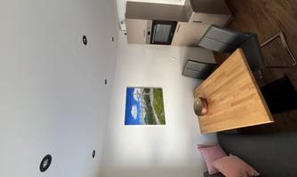A modern dining room with a wooden dining table and four chairs. A picture of a landscape hangs on the wall.