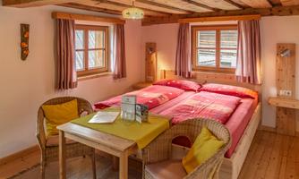 A cozy bedroom with a double bed and two chairs. Bright wood details and large windows create an inviting atmosphere.