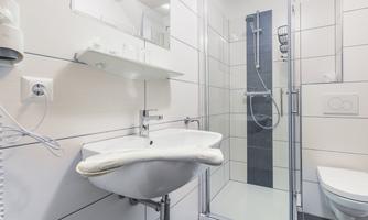 A modern bathroom with a shower cabin, a sink, and a toilet. The walls are in light colors, giving the room a clean appearance.