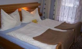 A cozy bedroom with a double bed and white pillows. A sheer curtain hangs in front of the window.