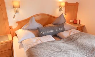 A cozy bedroom with a large bed and decorative pillows. The warm wooden paneling and soft lights create an inviting atmosphere.