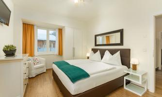 A modern bedroom with a large double bed and bright colors. The windows let in a lot of daylight and the decor is cozy and inviting.