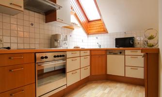 A modern kitchen with wooden cabinets and a large window. The room is bright and well-equipped.