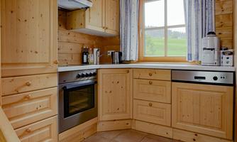 A cozy wooden kitchen with modern appliances. Through the window, one looks out onto a green landscape.
