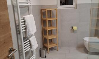 A modern bathroom with a towel warmer and a shelf cabinet. The design is bright and minimalist, featuring large tiles and clean lines.