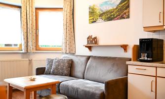 A cozy living room with a gray sofa and a wooden table. A landscape picture hangs on the wall, and there is a coffee machine in the room.